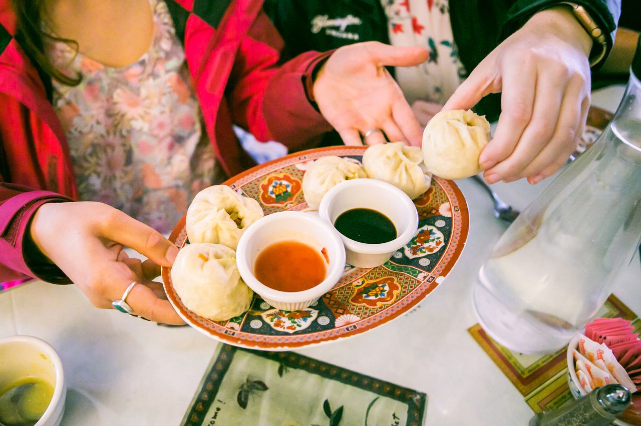 Hands holding a plate with dumplings and dipping sauces