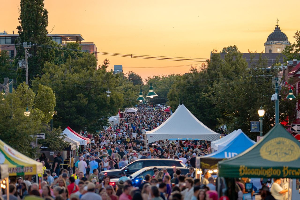 A bustling outdoor festival in Bloomington Indiana with crowds attending under tents during sunset