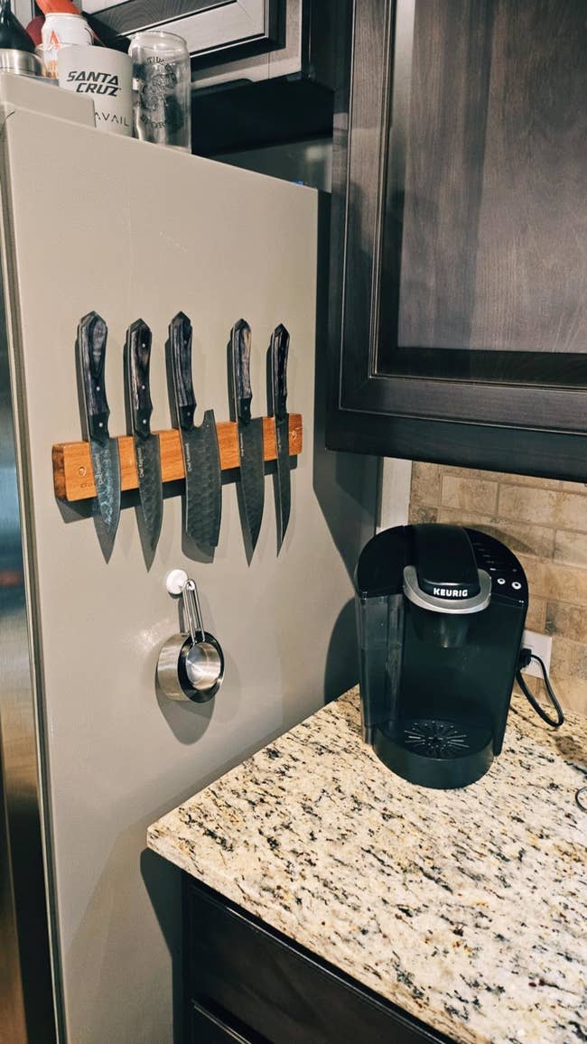 Kitchen countertop with a Keurig coffee maker and a magnetic knife holder displaying five kitchen knives on the side of a fridge