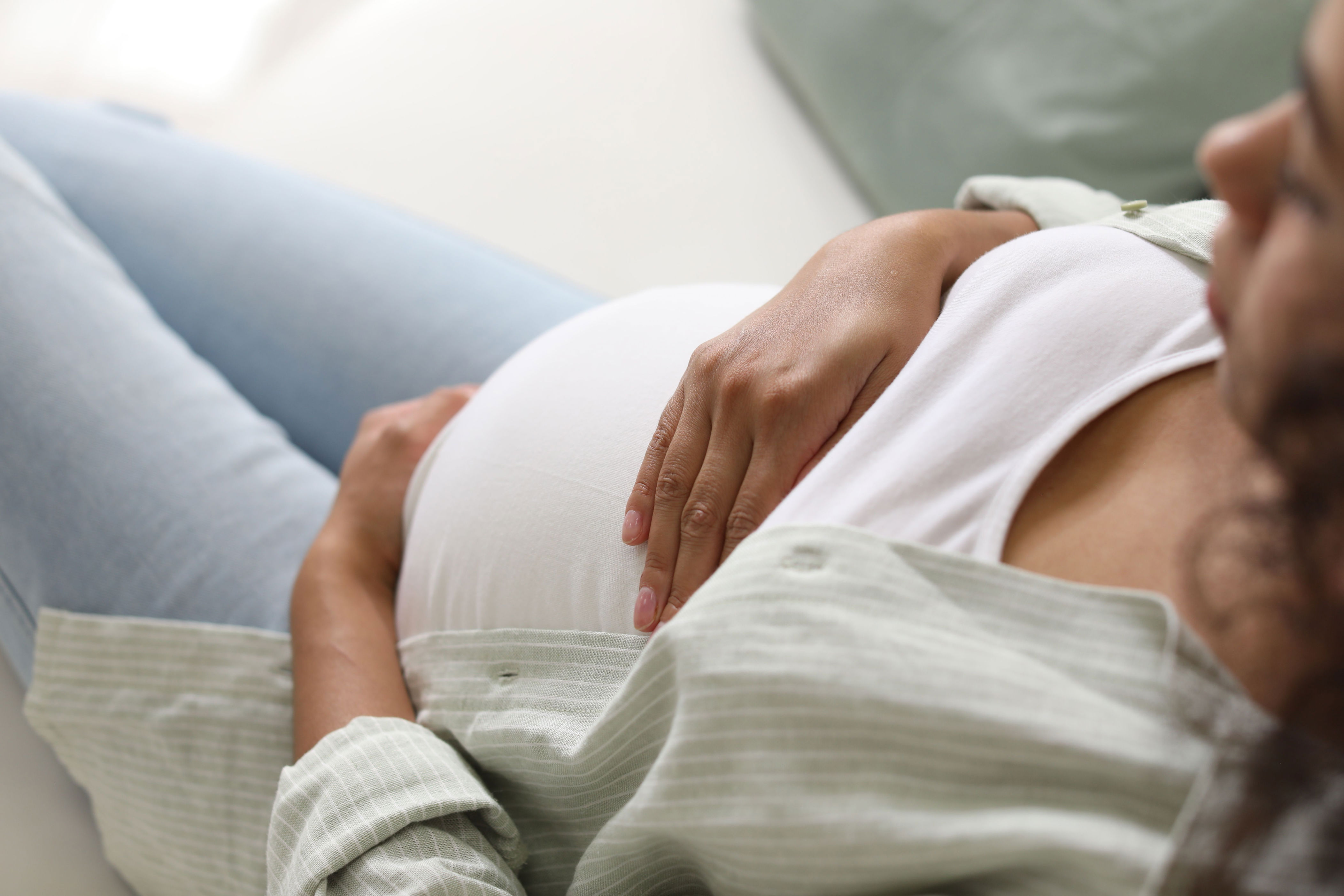 Pregnant person relaxing, lying back with hands resting on the belly, wearing a white top and unbuttoned shirt