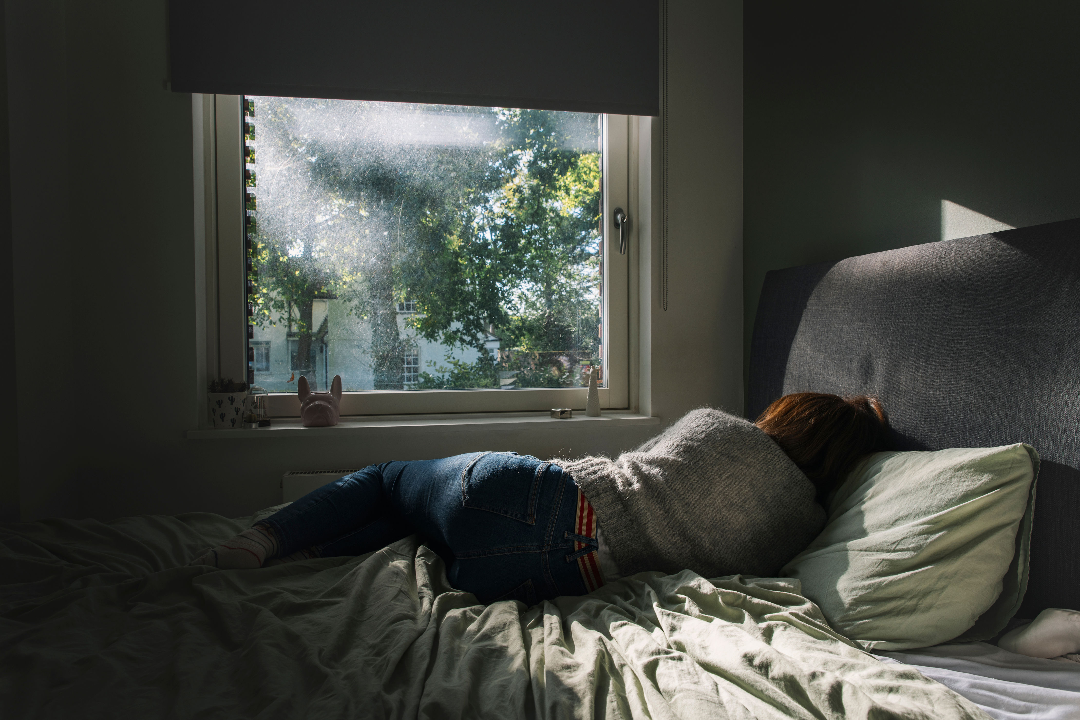 Person lying on a bed in a dimly lit room with sunlight streaming through a window, creating a peaceful atmosphere