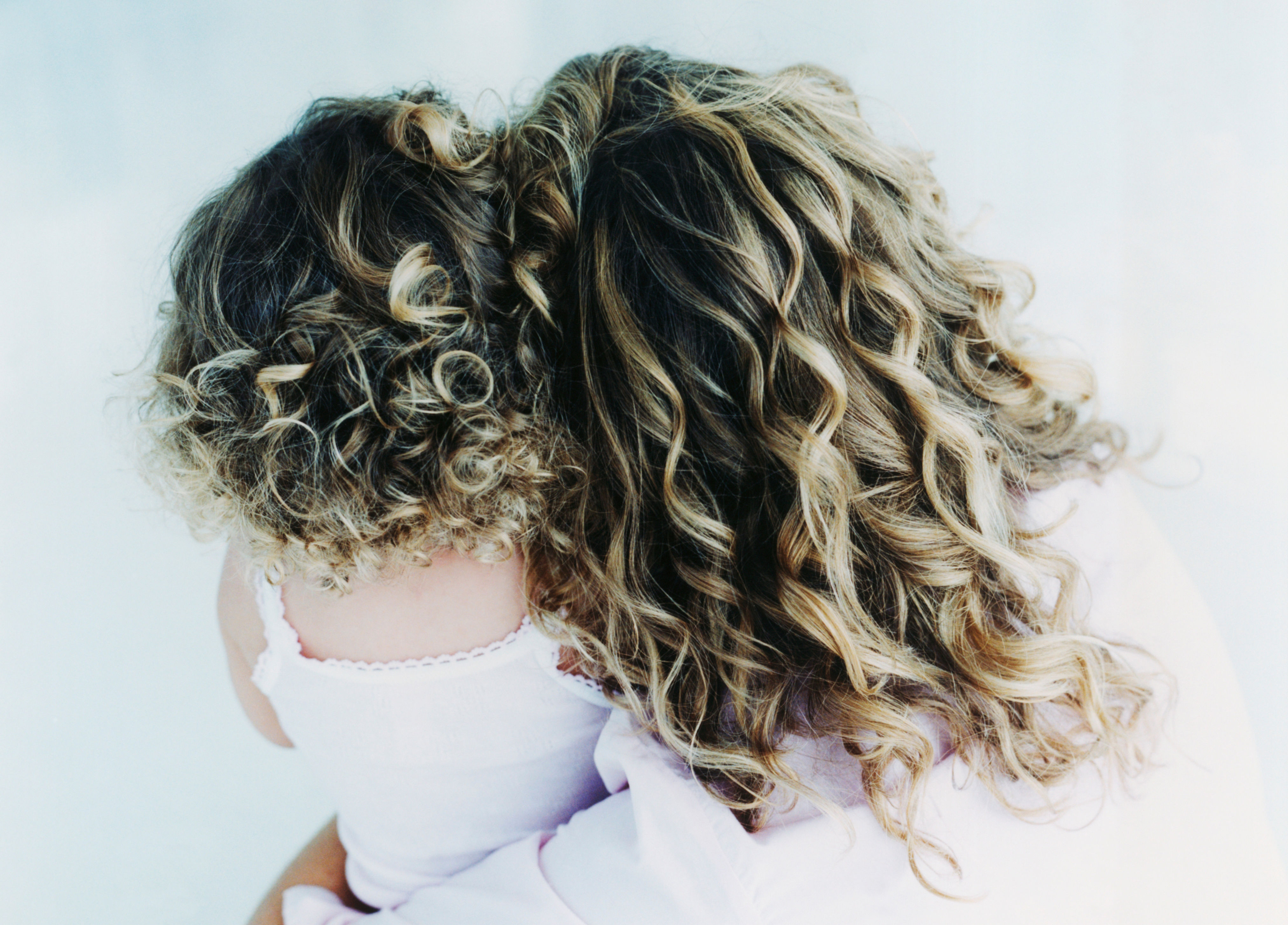 Two people with curly hair, viewed from behind, embracing each other lovingly