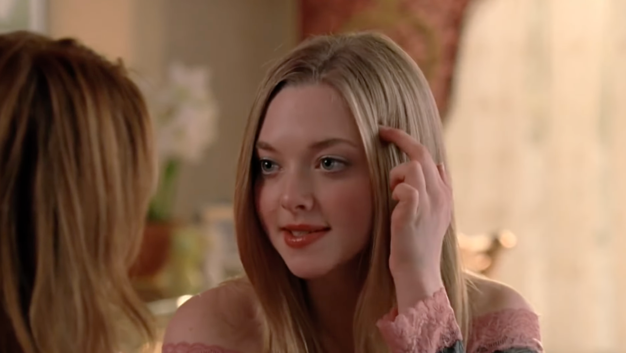 A person is seated indoors, gesturing with their hand near their head while engaged in a conversation with someone off-camera