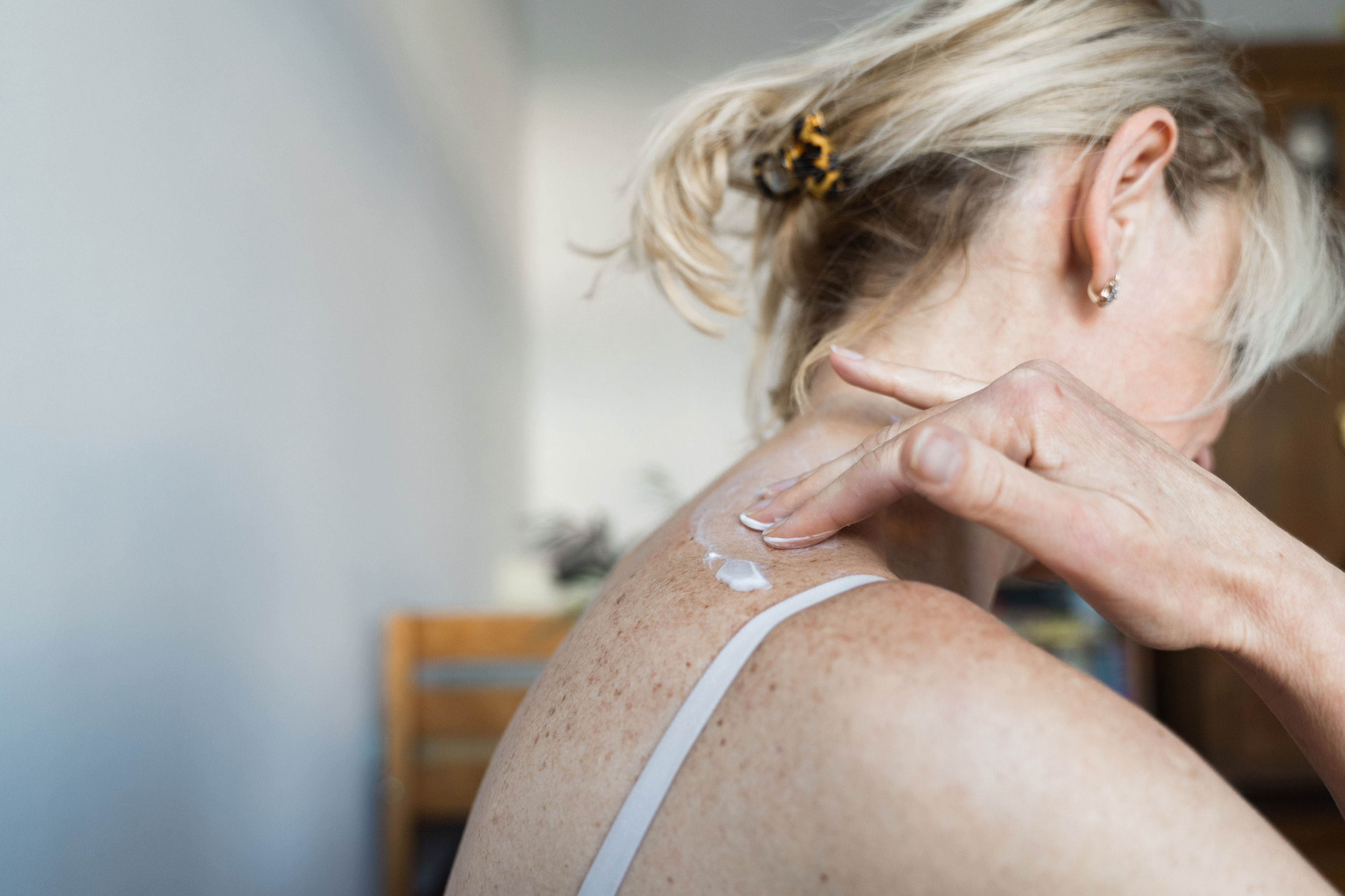 Person applying cream on their shoulder, focusing on skin care. Hair is tied back with a clip