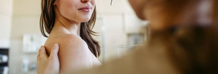 A woman undergoing a mammogram, looking at a medical professional for reassurance