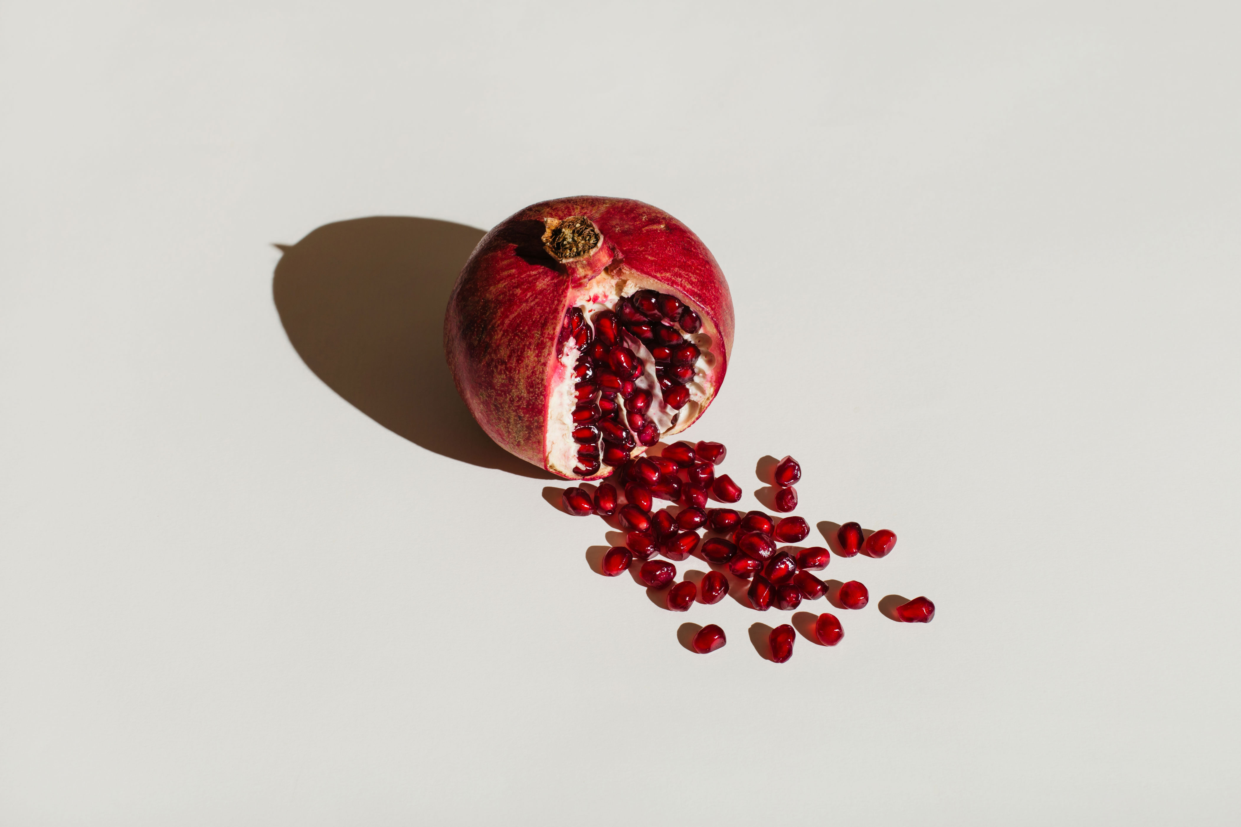 Pomegranate with seeds spilling out on a plain surface