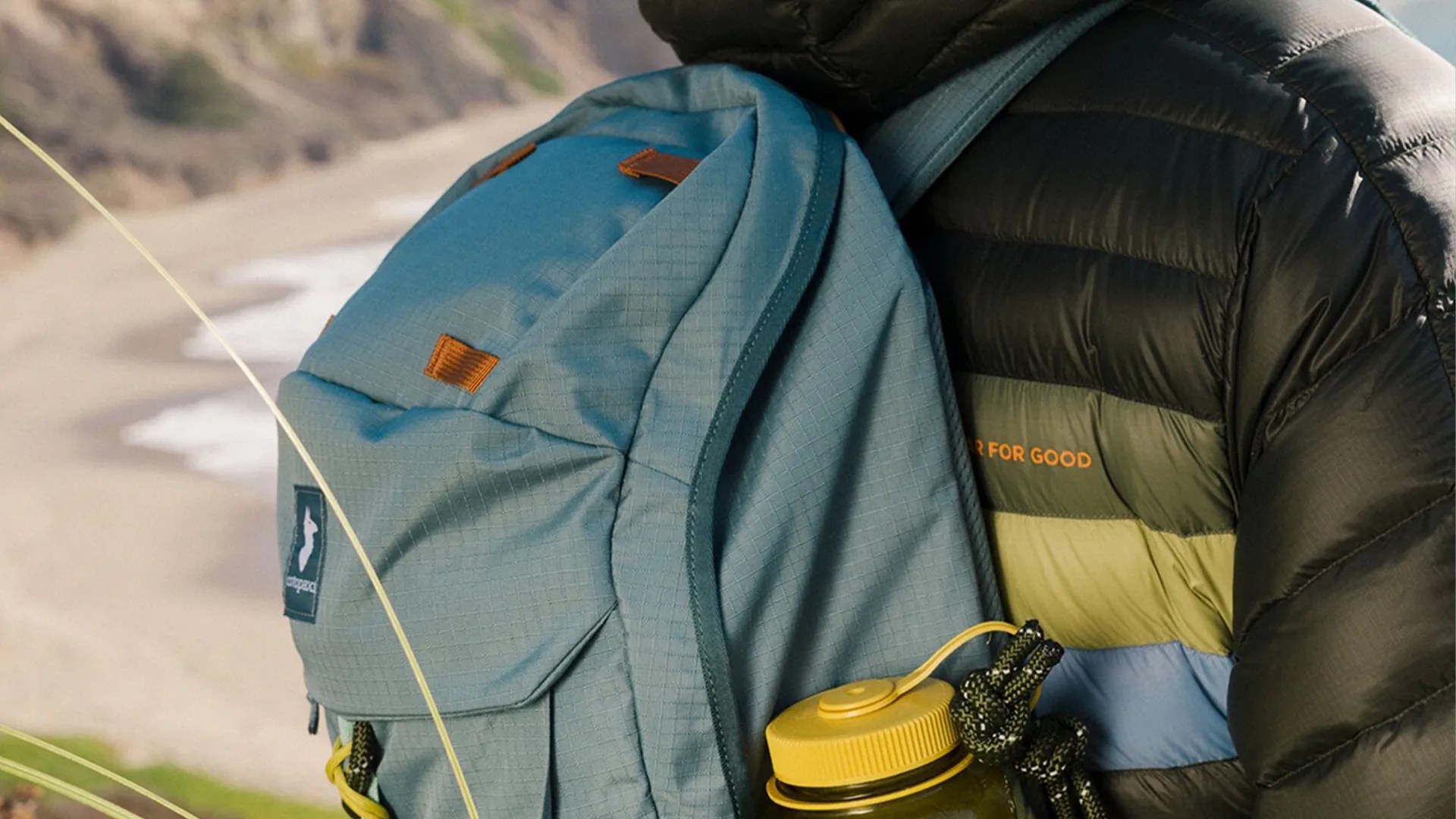 Blue Patagonia backpack with leather accents and a yellow water bottle in the side pocket worn by a person in a puffer jacket.