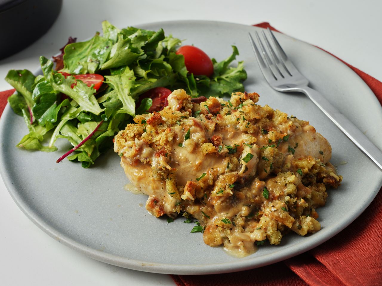 Plated chicken with stuffing topping and green salad with red napkin