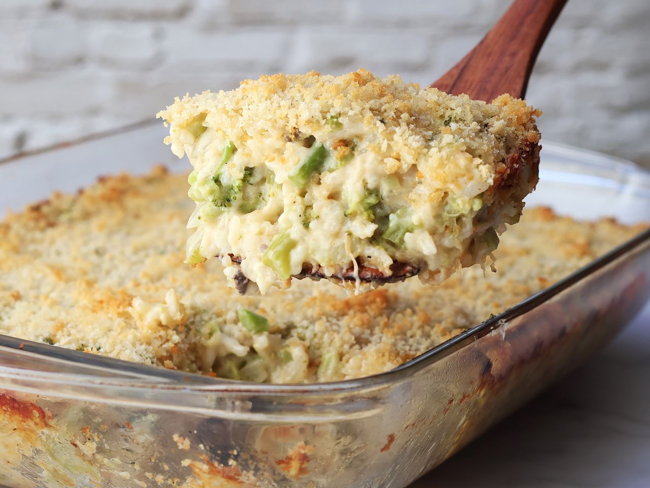 Broccoli Rice Casserole scoop on a wooden spatula over a glass baking dish