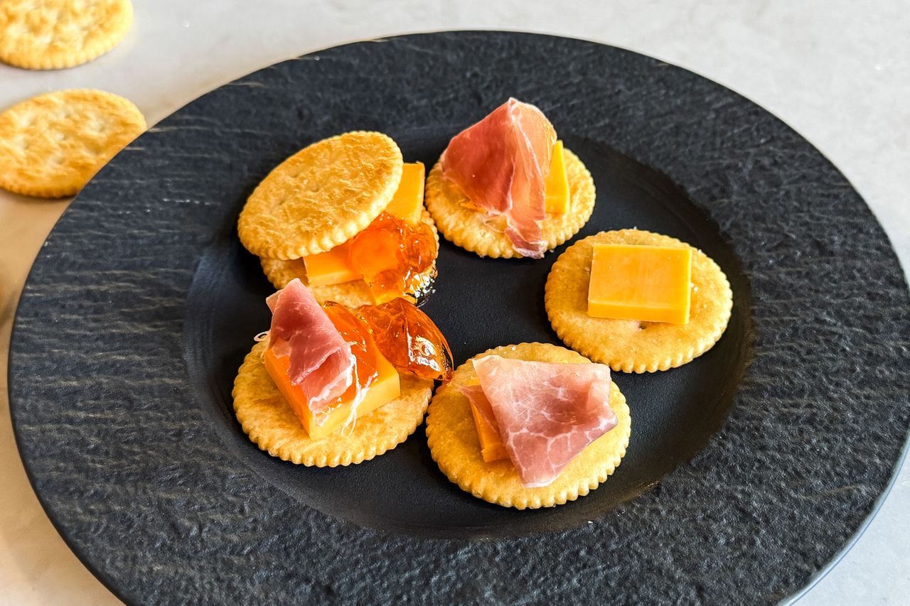 Crackers topped with cheese and prosciutto served on a dark plate
