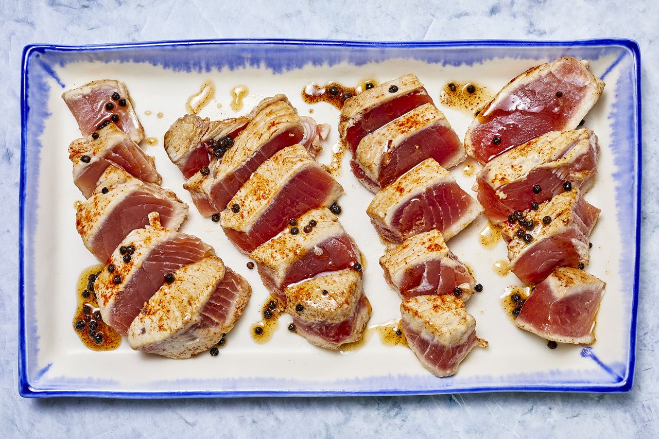several medium rare seared tuna steaks are sliced on a blue and white platter.