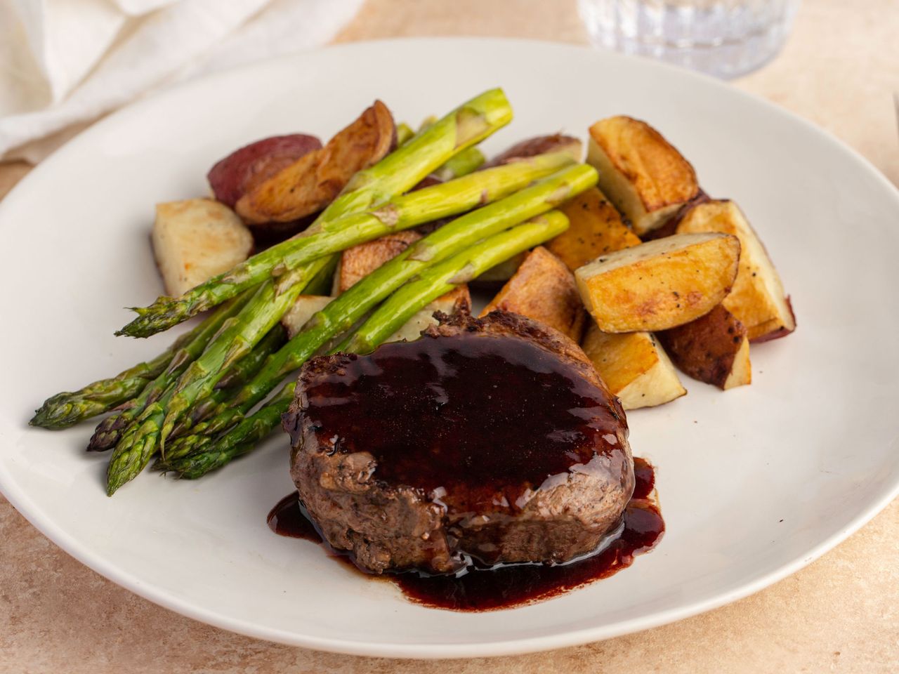 A plate with beef filet covered in balsamic sauce roasted potatoes and asparagus spears