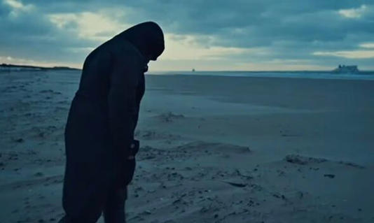 Mariam looks out across the sea towards the UK at dusk from a shoreline in France