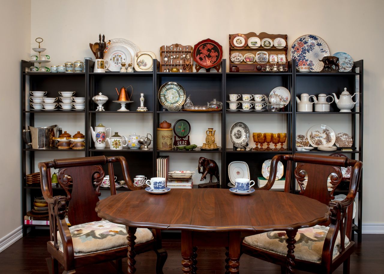 Dining table in front of a shelf displaying various plates cups and decorative items