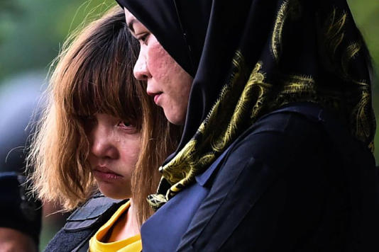 Two individuals are standing side by side, with one person wearing a black hijab and the other person donning a yellow shirt. Both individuals appear to be focused on something in front of them.
