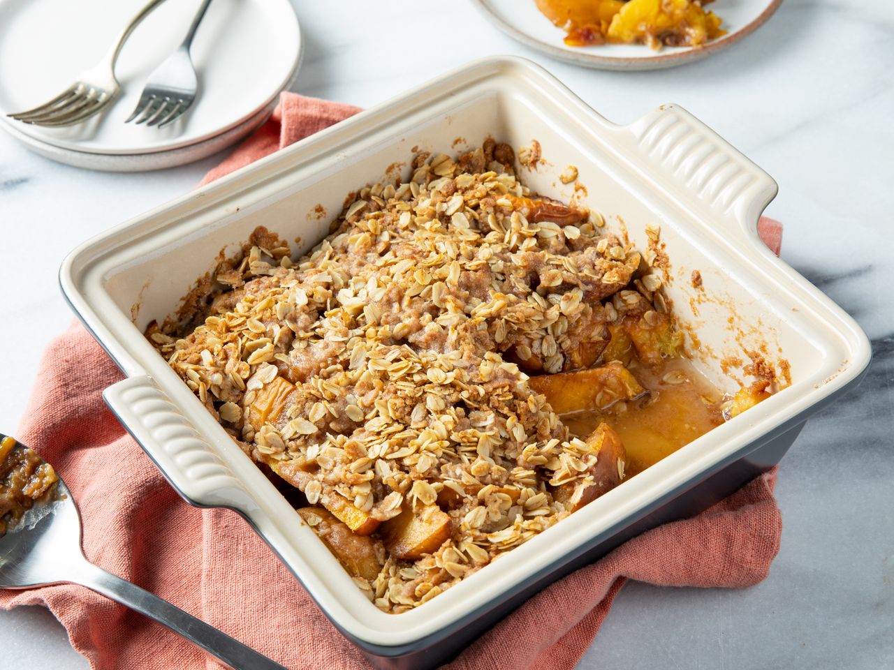 a high angle view looking over the a square white baking dish of Mom's Peach Crisp with a scoop out.