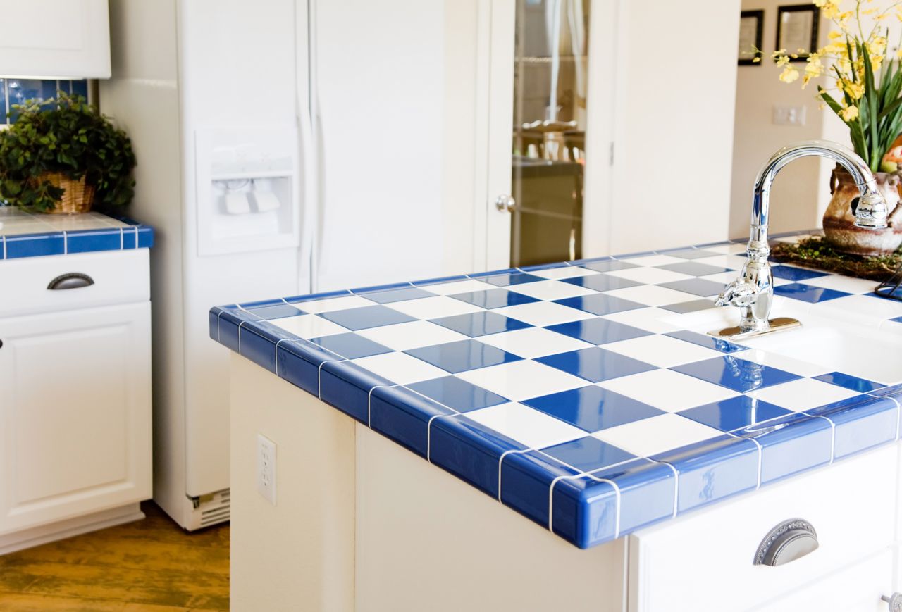 A kitchen countertop with a blue and white tiled surface and a faucet