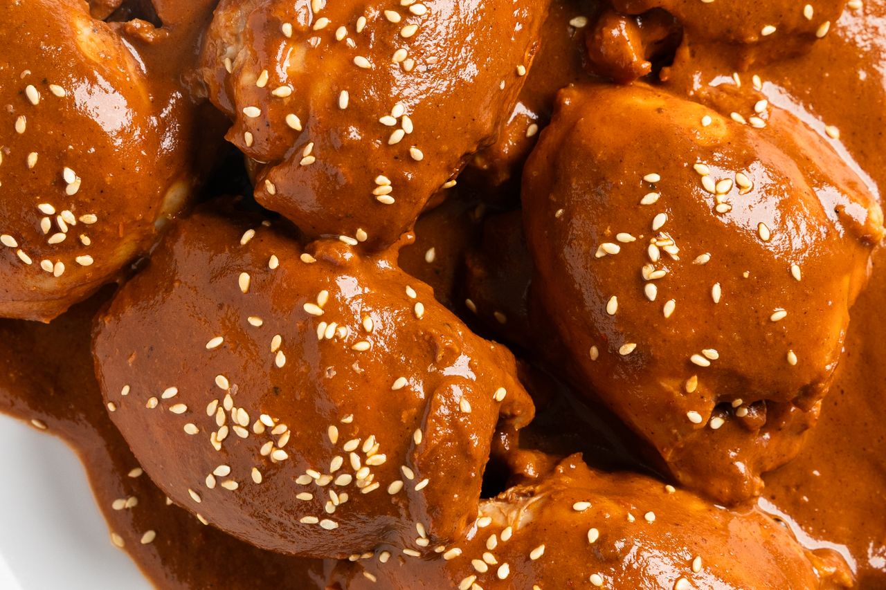 Chicken thighs covered in mole sauce sprinkled with sesame seeds