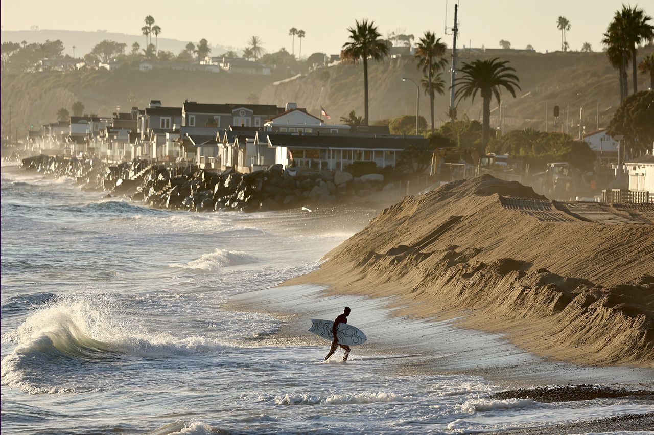 Surfer walking on a beach with waves and shoreline houses in the background