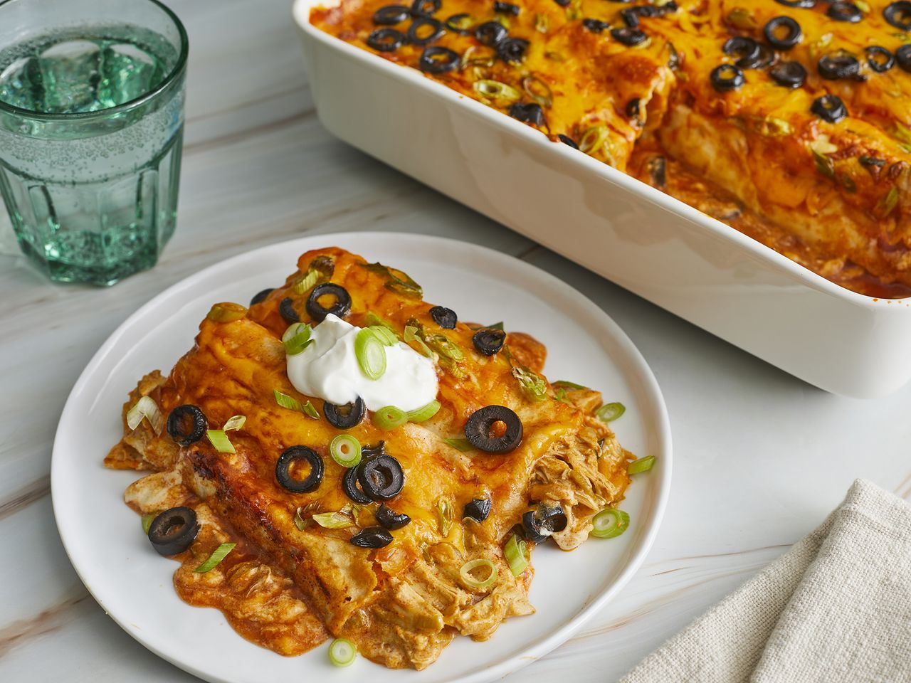 close up on a serving of enchiladas on a plate with remaining in a casserole dish behind