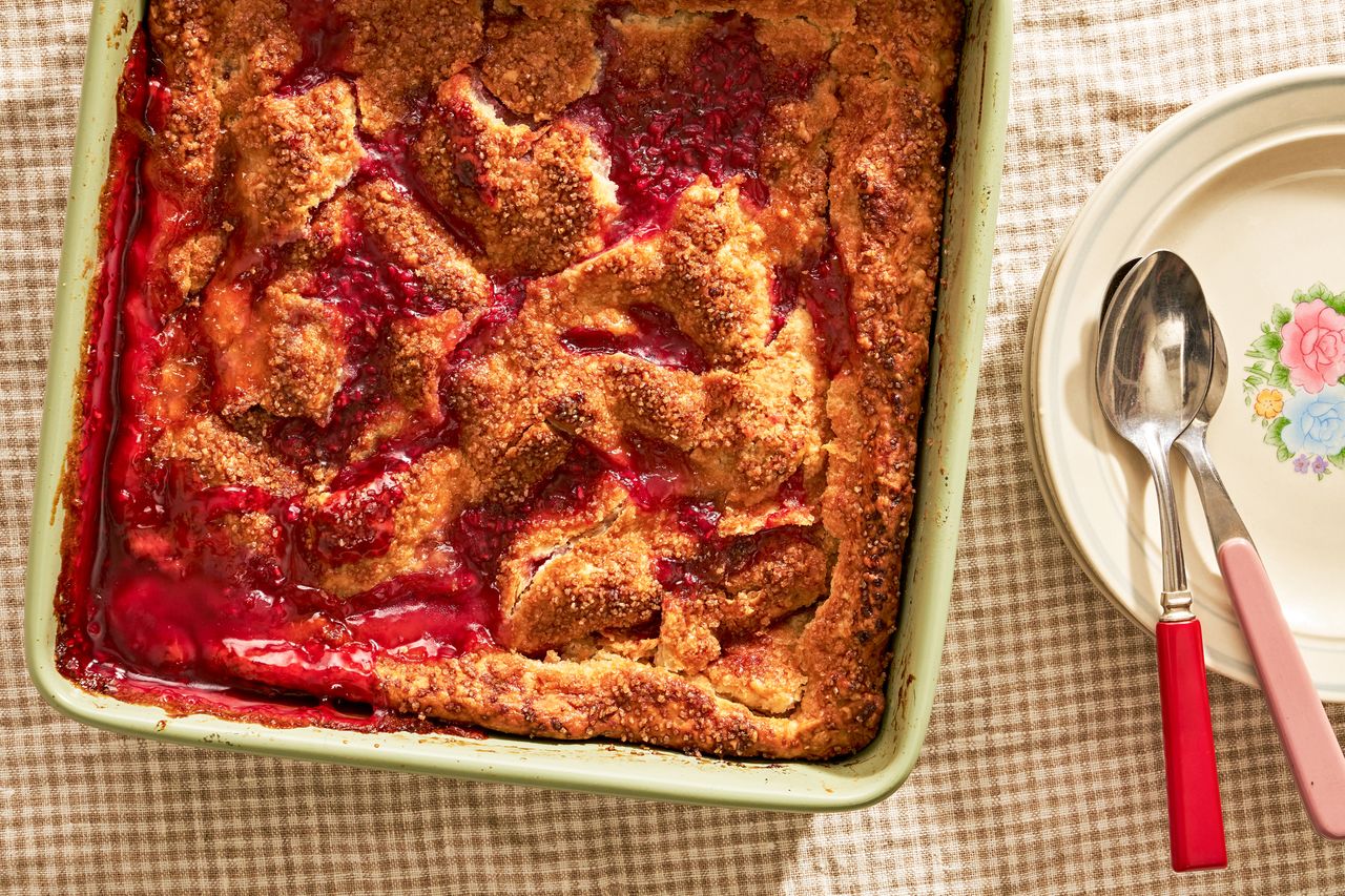 peach and raspberry pandowdy in a casserole dish next to a stack of plates on comfy (cottage-core style) table
