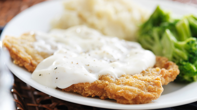 A macro shot of chicken fried steak served with white gravy, broccoli, and mashed potatoes