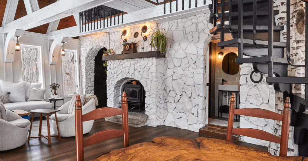 White stone fireplace and exposed white beams inside a Switzerland-inspired A-frame in North Kingstown, RI.