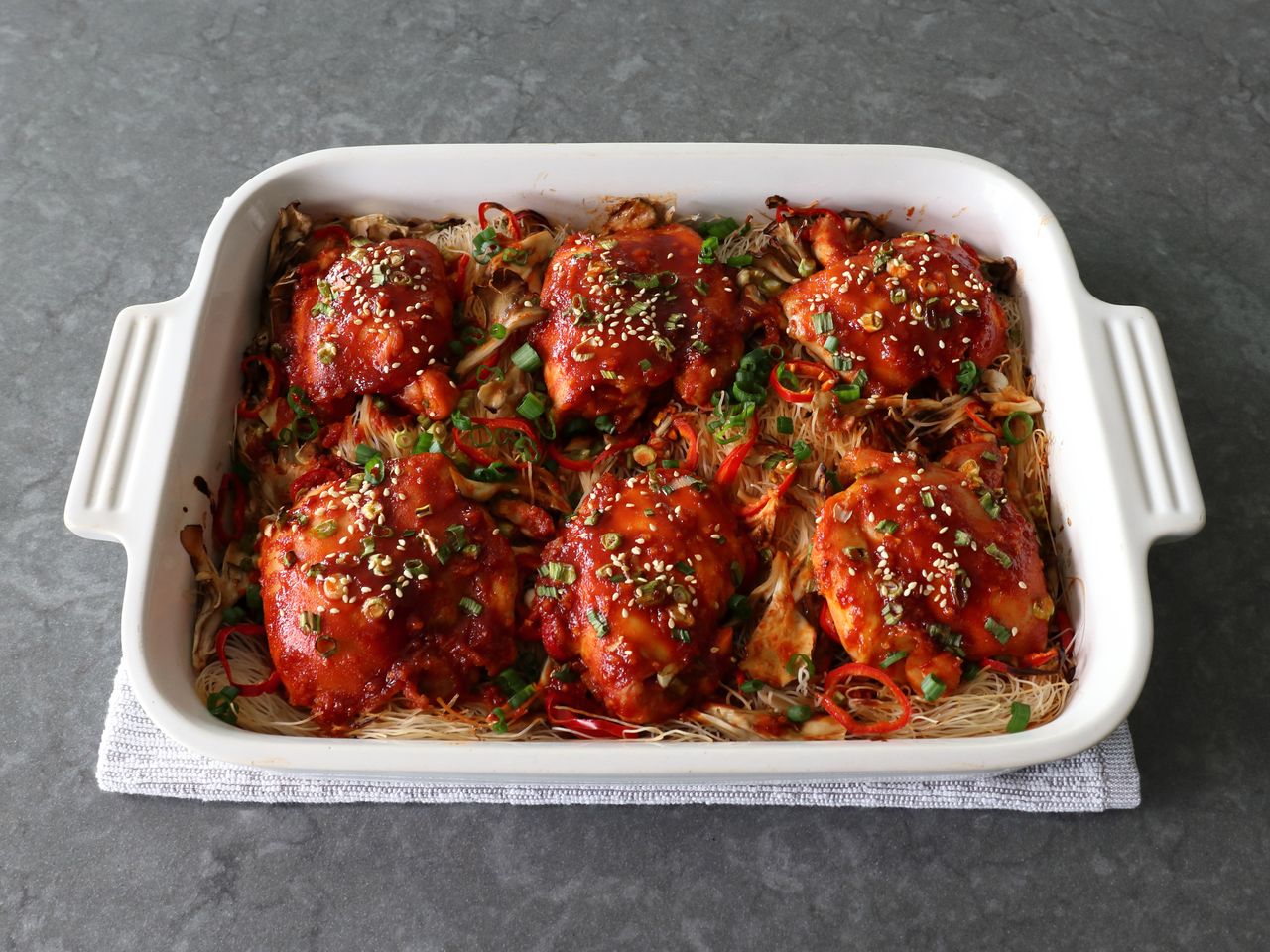 white casserole dish with 6 spicy chicken thighs over rice vermicelli