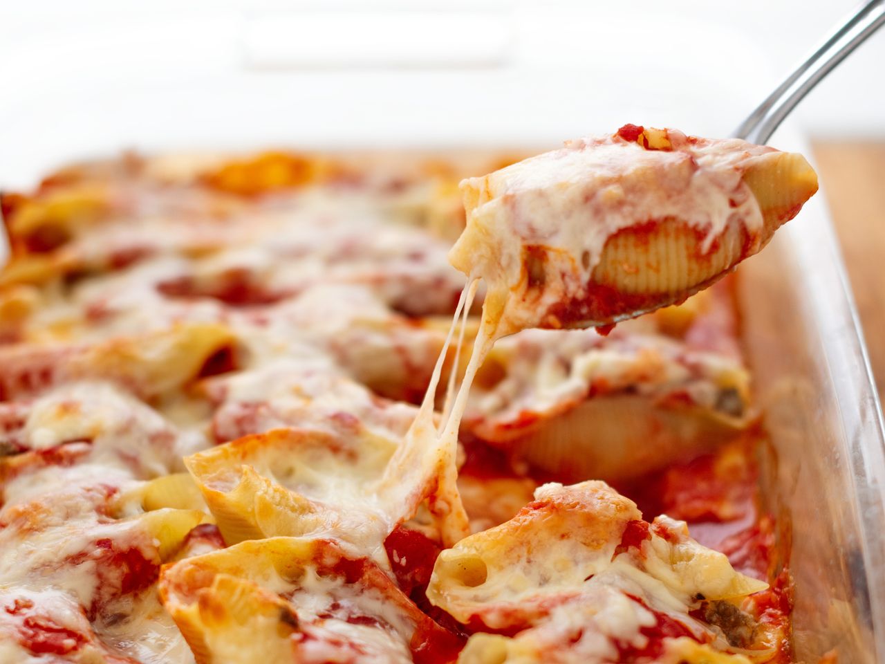 Glass casserole dish of stuffed shells with melted cheese showing one spoonful up close
