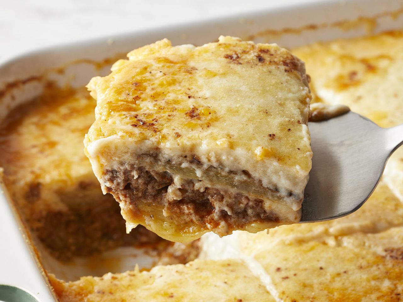 mid angle looking at a casserole dish of moussaka with a serving being pulled out