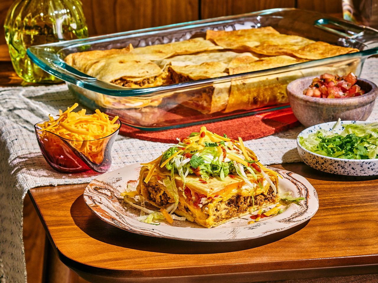 A CrunchWrap Casserole sitting on a wood table with a serving of the casserole on a plate.