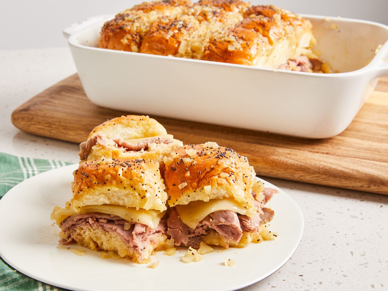 close up on a few Hawaiian rolls roast beef and cheese sandwiches on a plate with remaining in baking dish behind