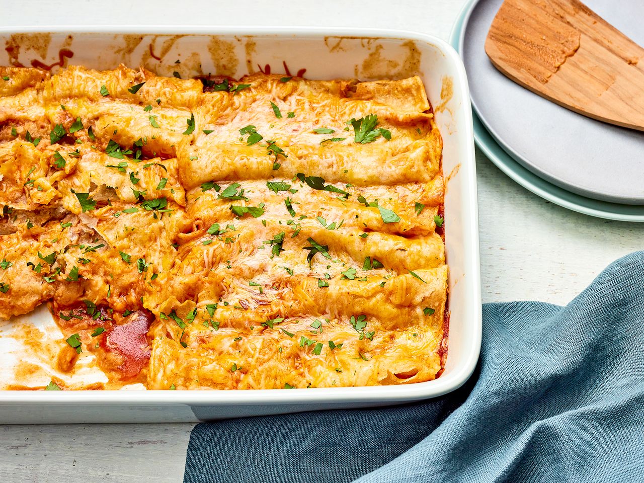 Refried Bean and Cheese Enchiladas garnished with fresh herbs in a white baking dish