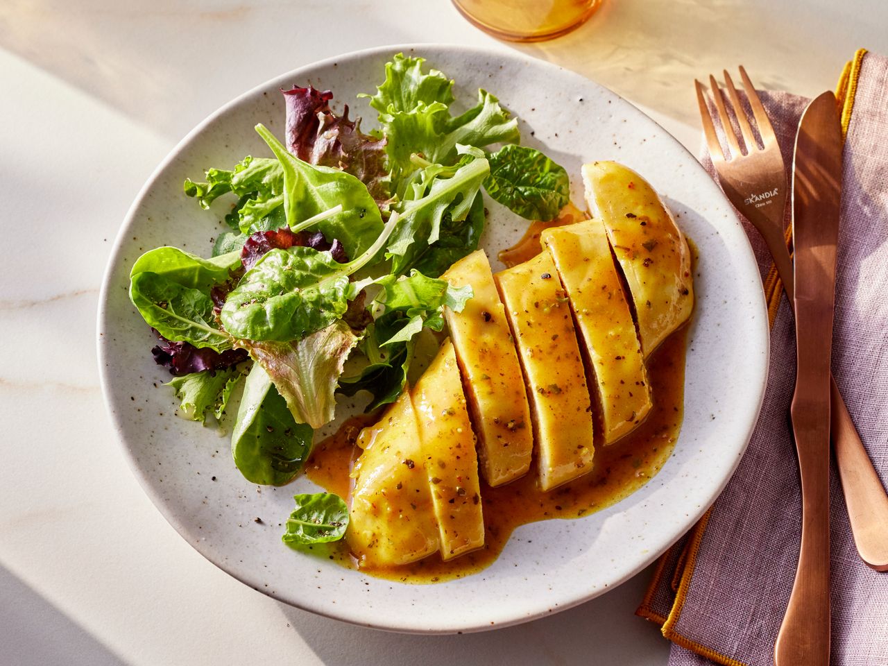 A plate of sliced baked honey mustard chicken served with a salad of mixed greens