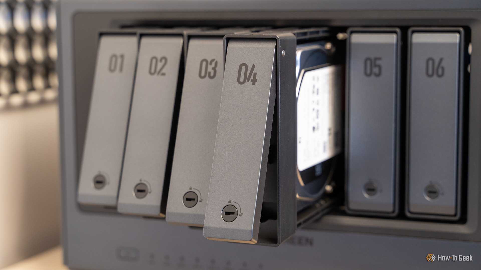 Drive trays fanned out from the Ugreen iDX6011 Pro NAS showing the tool-free tray design and an installed hard drive.