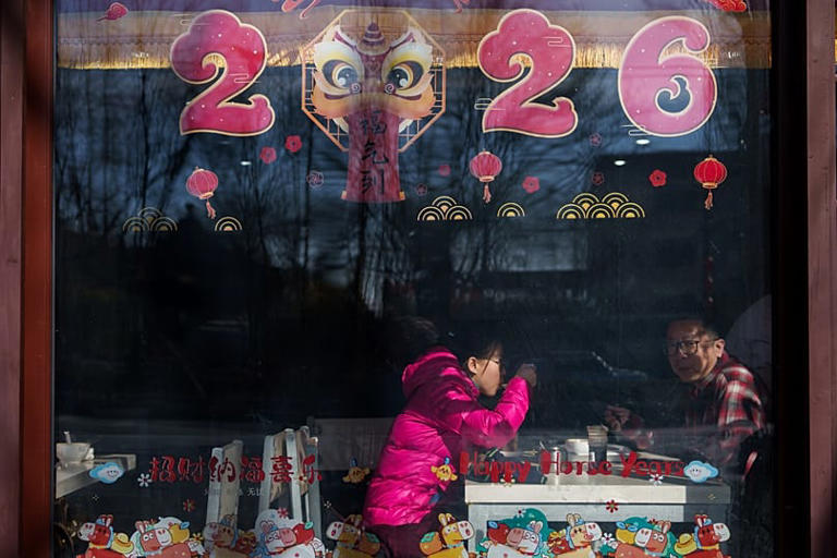 Un hombre mira por una ventana decorada con "2026" y adornos festivos del Año Nuevo Lunar en Pekín, China, el lunes 16 de febrero de 2026. (AP Photo/Vincent Thian) AP Photo