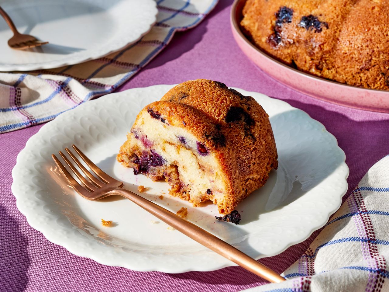 Blueberry sour cream coffee cake slice on a white plate with fork, ready to serve.