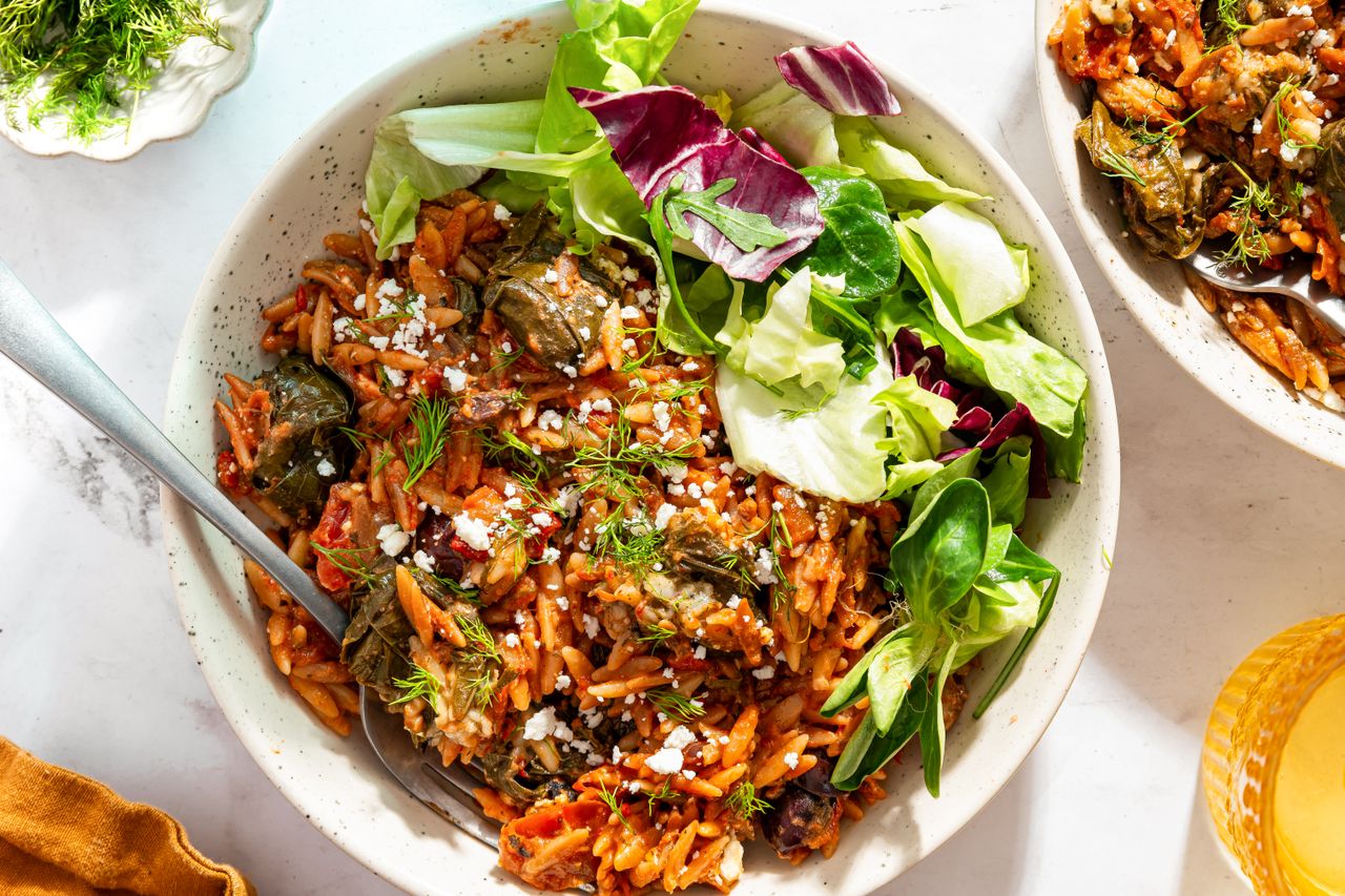 Bowl of orzo and dolma mixed with tomato sauce accompanied by fresh greens
