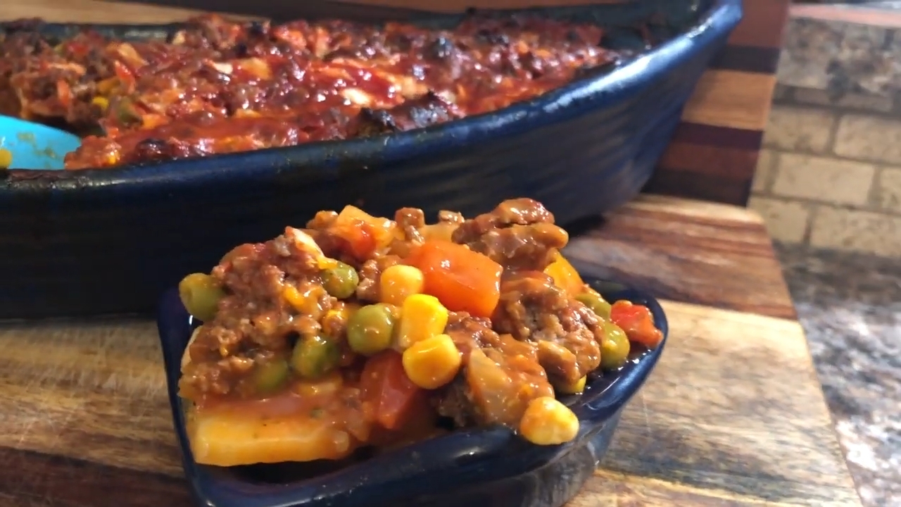 Baked casserole with ground meat, corn, peas, and carrots in a dish on a wooden surface