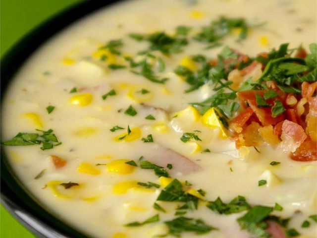 close up view of Slow Cooker Corn Chowder garnished with bacon and fresh herbs in a bowl