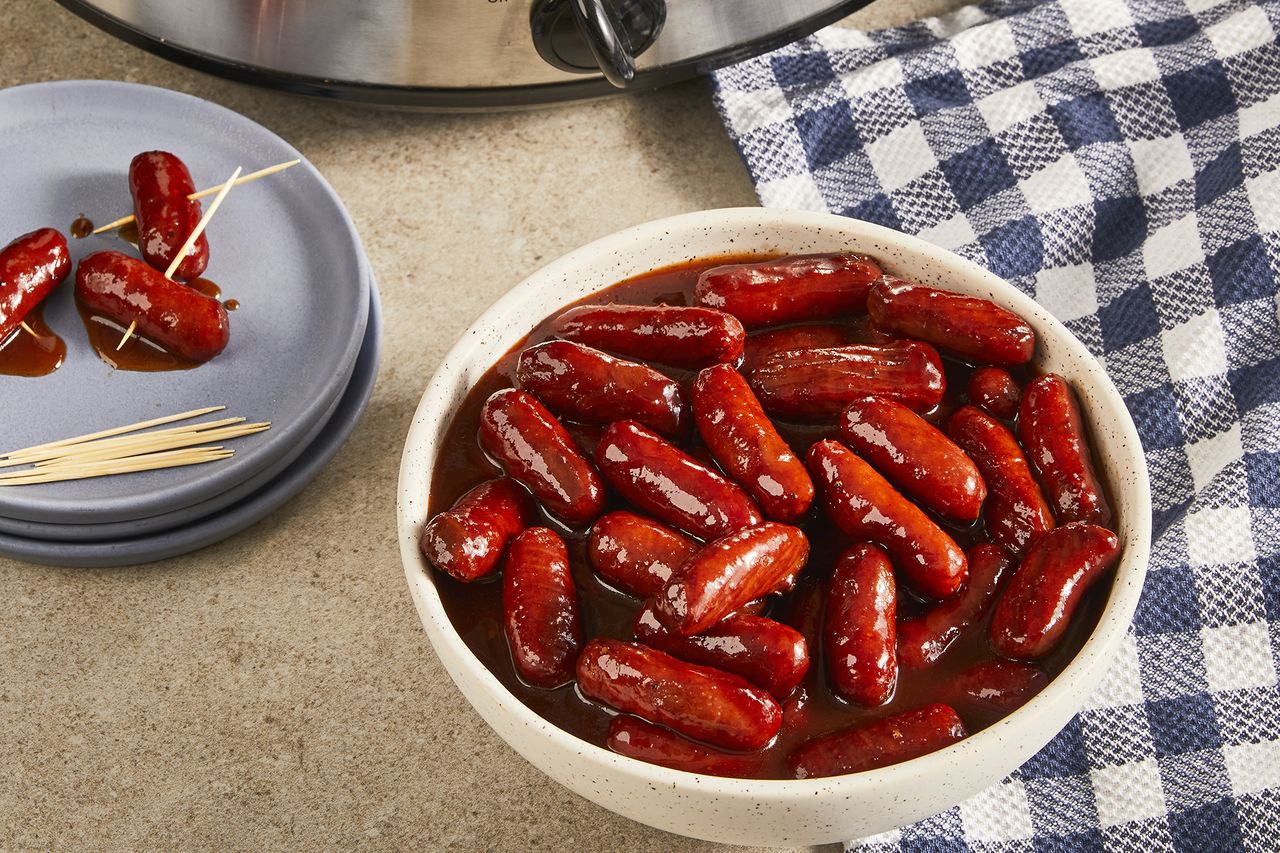 a close up view of a bowl of slow-cooker cocktail smokies. A slow cooker sits in the background