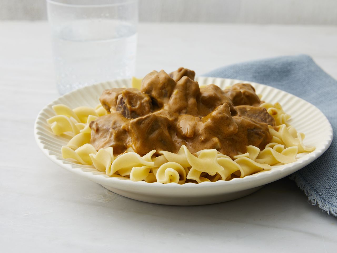 mid angle, looking at a white plate of egg noodles topped with beef stroganoff