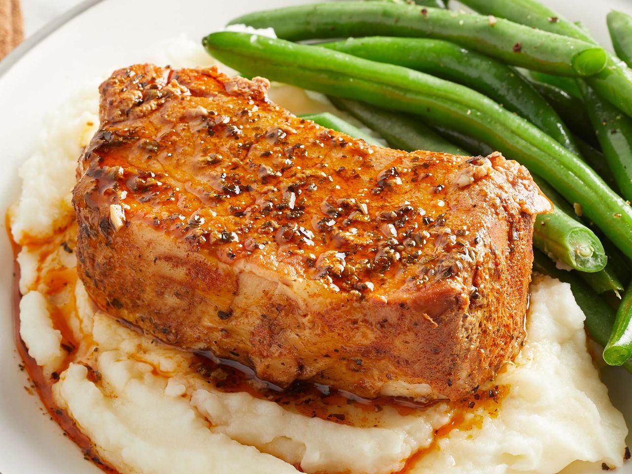 mid angle looking at slow cooker pork chops on top of mashed potatoes,served on a plate with a side of green beans