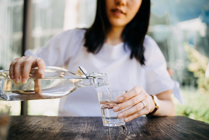 Woman Pouring Water From Bottle Into The Glass At A Outdoor Cafe