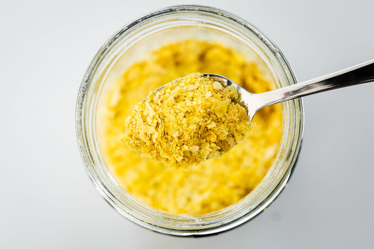 pantry staple close-up, spoonful of nutritional yeast over clear glass jar shot from above, daily ingredients