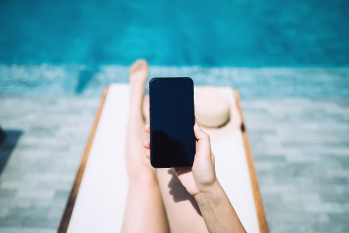 Low Section Of Young Woman Using Smartphone While Enjoying The Sun On Lounge Chair By The Pool Side