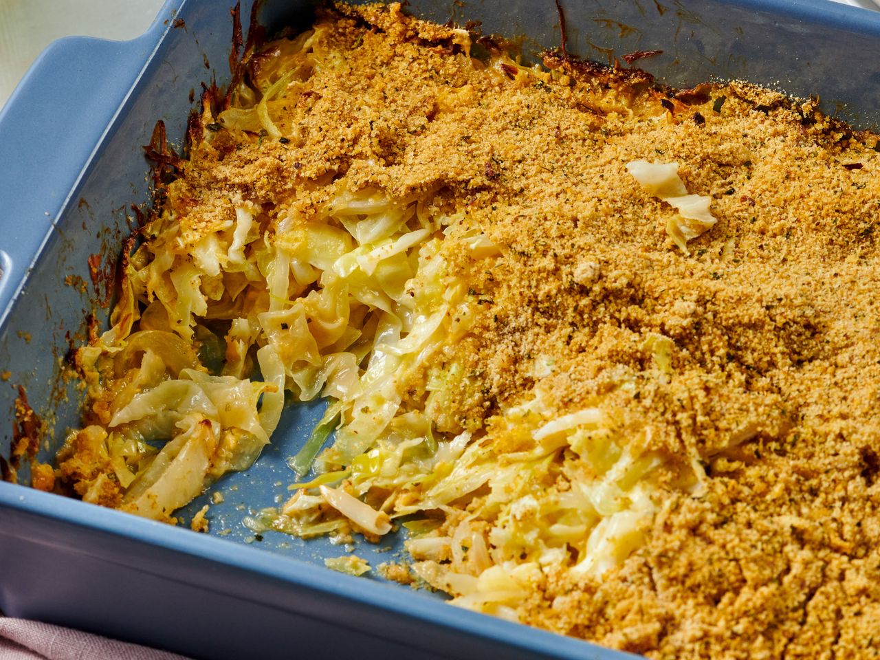 A tray of cabbage casserole with a portion removed showing shredded cabbage and baked topping in a square dish