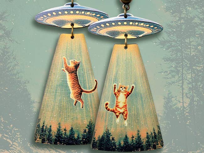 Earrings featuring UFOs beaming up playful cats in a whimsical forest scene