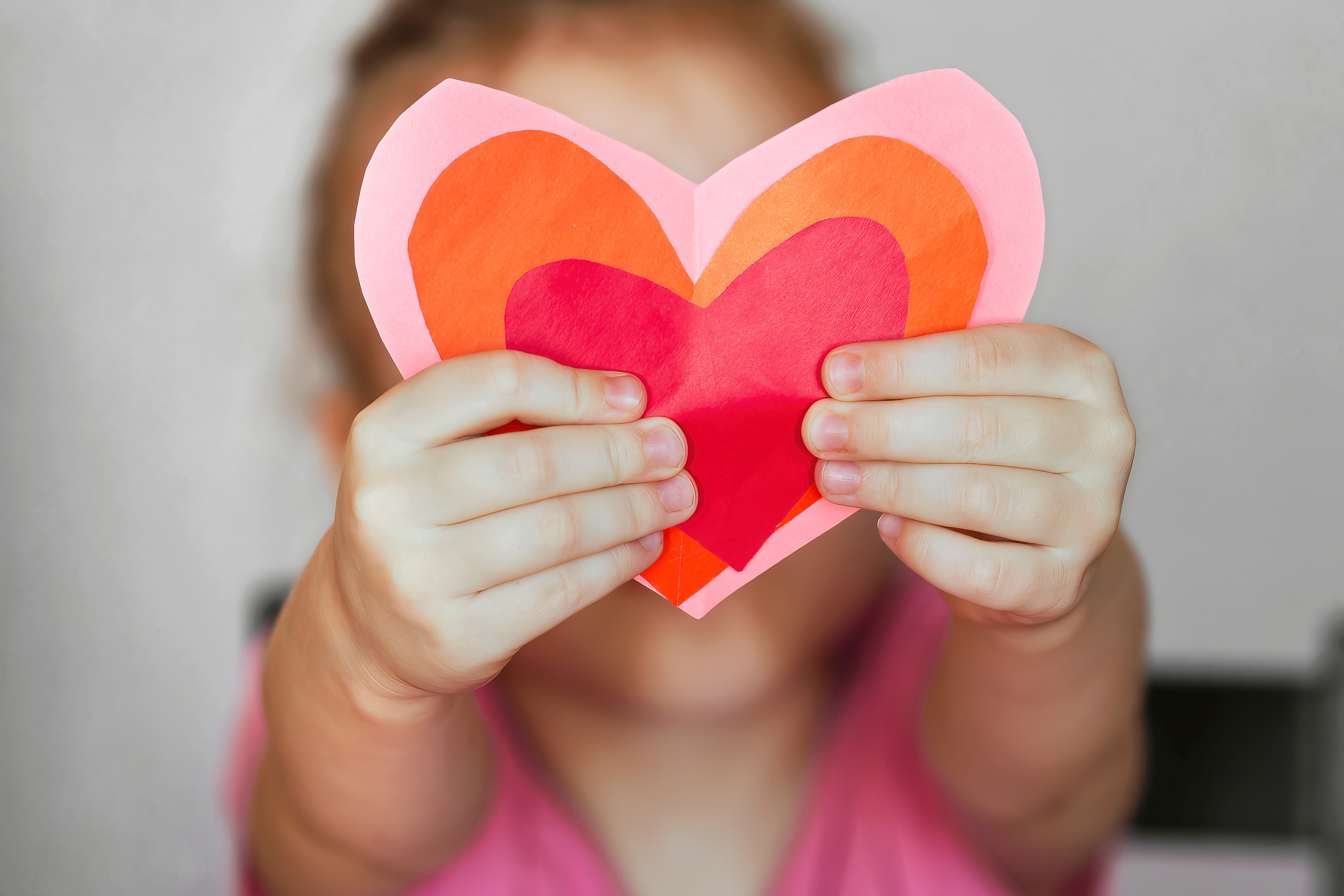 Child holding layered paper hearts in front of face