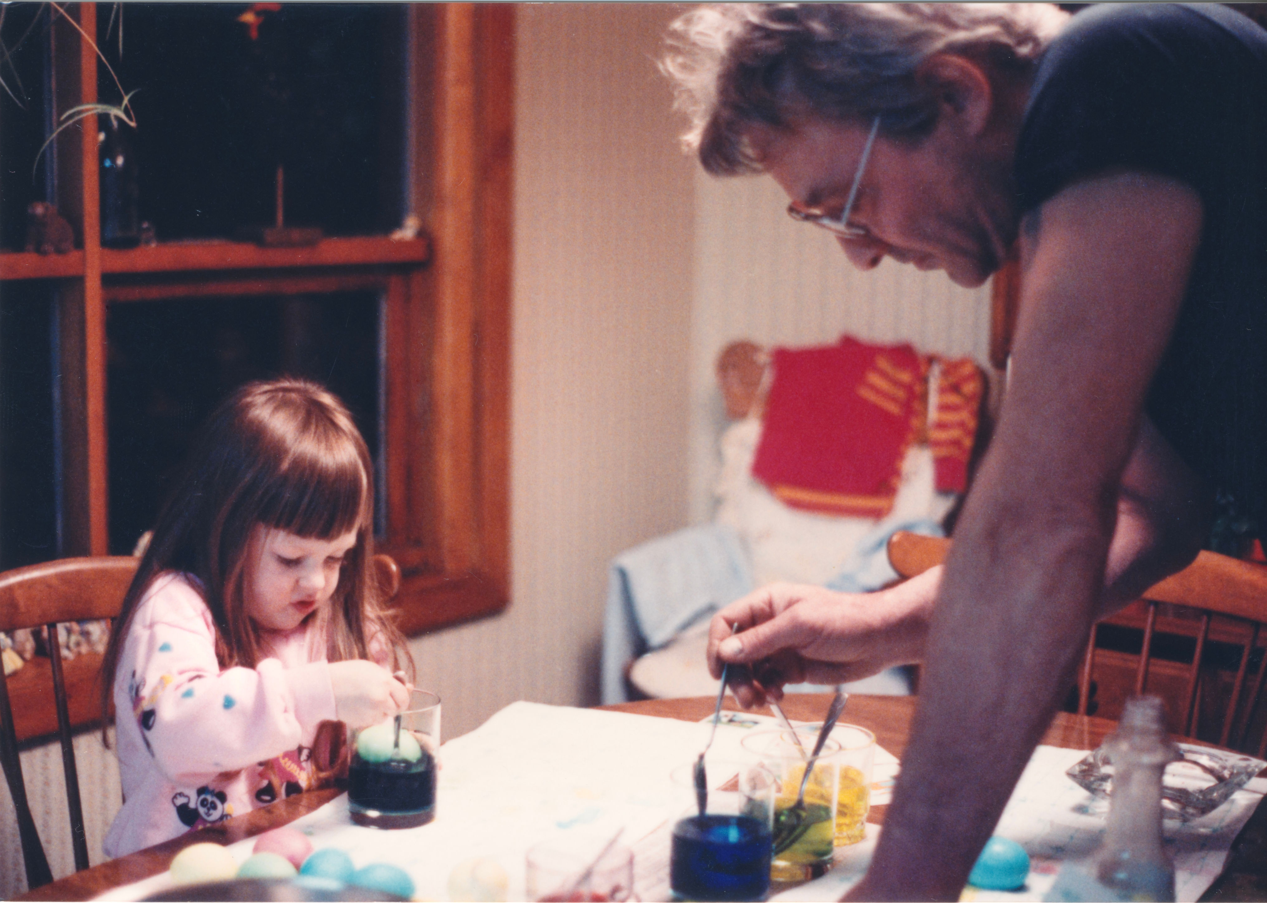 Child and older adult dyeing Easter eggs at a table, focused on their activity